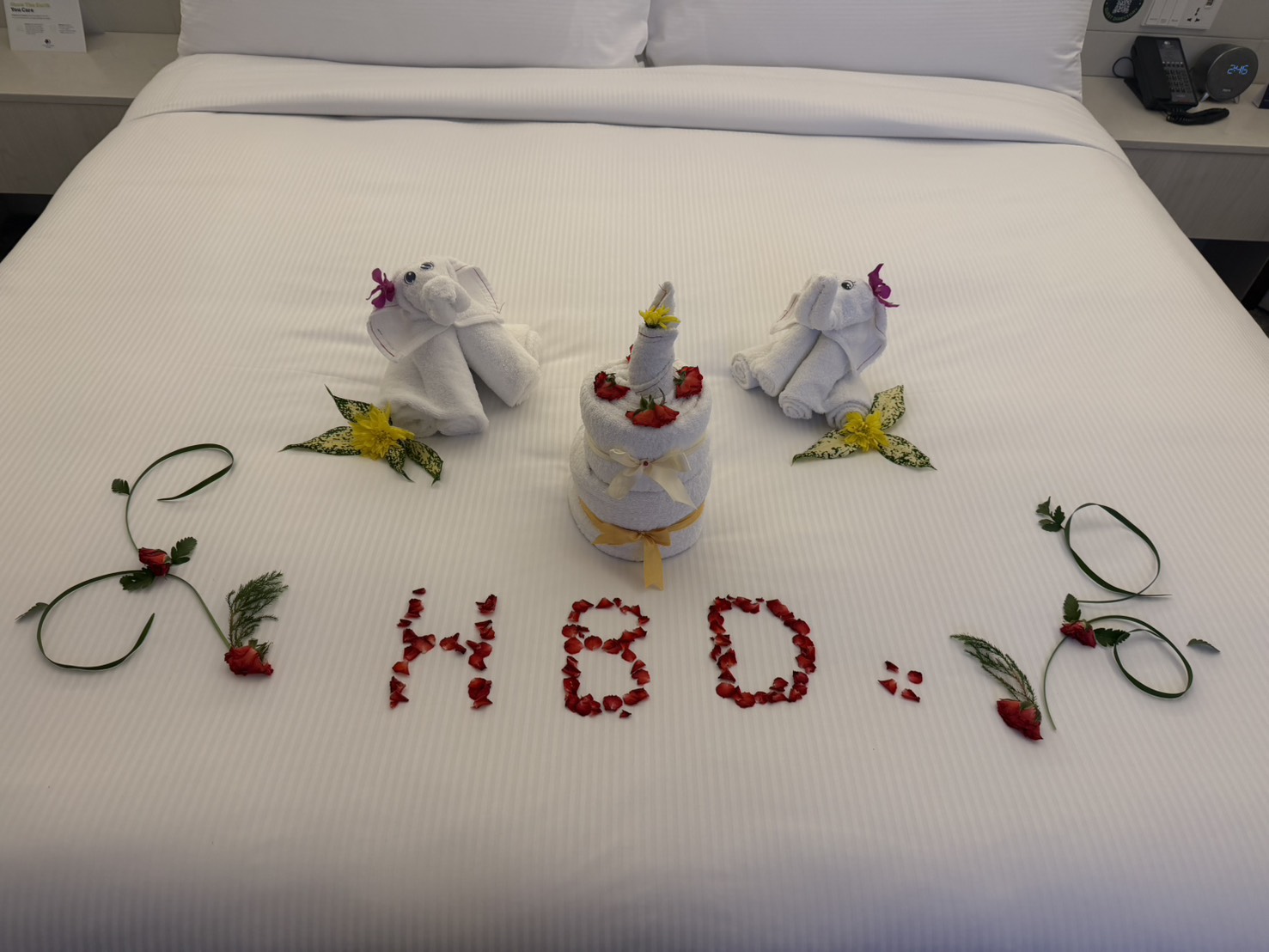 整張床鋪滿心意——毛巾小象、毛巾蛋糕,還用玫瑰花瓣排出「HBD」